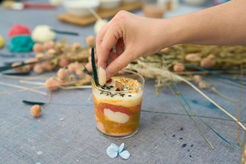 A hand stirring a layered drink with a straw in a glass, surrounded by scattered objects on a table. 3