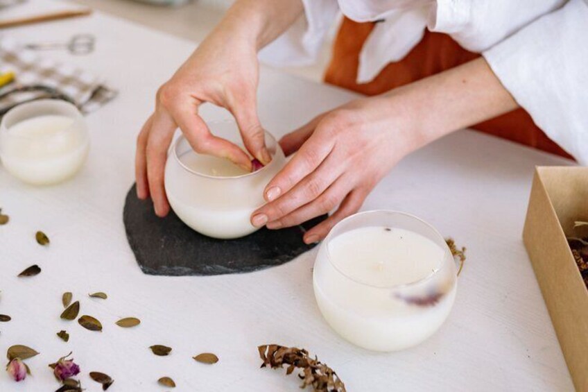 Hands mixing a white substance in a bowl on a white surface with scattered seeds and a glass of white liquid nearby. 1