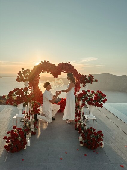 A couple at a seaside wedding ceremony with a heart-shaped floral arch and candles. 1