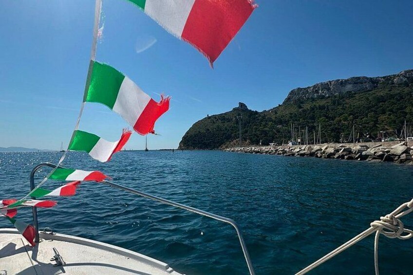 A boat with Italian flags, calm sea, rocky coastline, and a clear sky. 2
