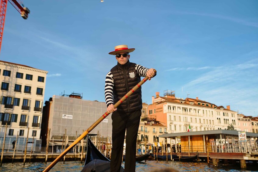 A gondolier in a striped vest and straw hat, holding a gondolier's pole, standing on a gondola in Venice. 3