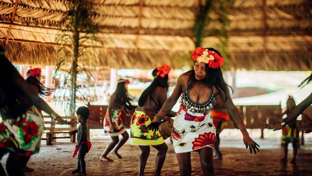 A group of people in traditional attire dancing under a thatched roof. 3