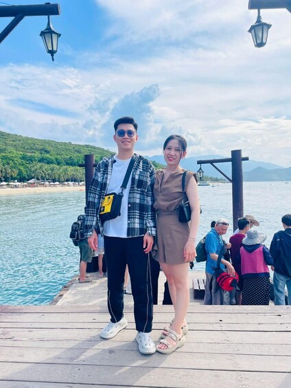 A couple standing on a wooden pier with a lake and mountains in the background. 2