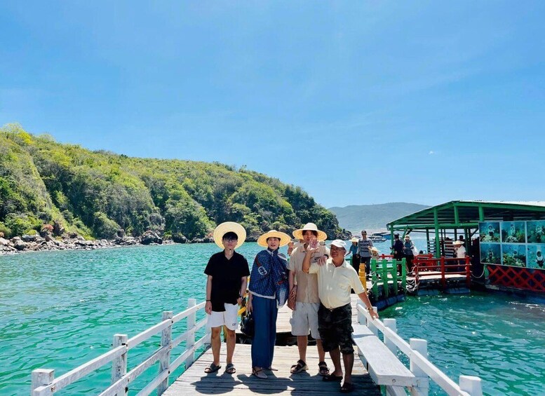 A group of people on a wooden pier with a green boat and a mountainous backdrop. 5