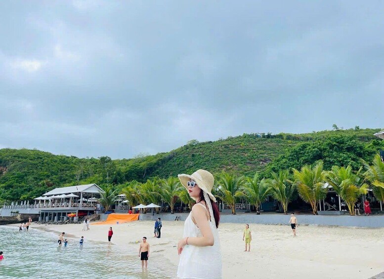 A beach with people swimming and walking, palm trees, and a hill in the background. 4
