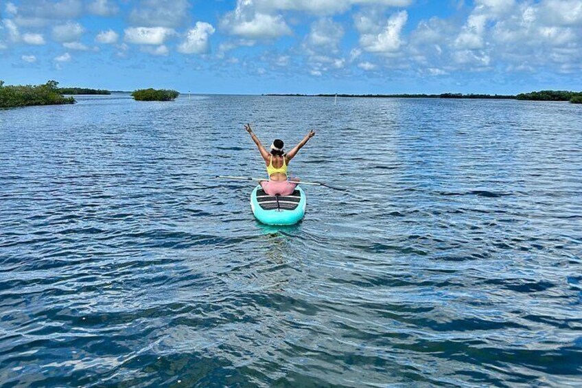 A person sitting on a paddleboard in calm water with a clear sky. 1