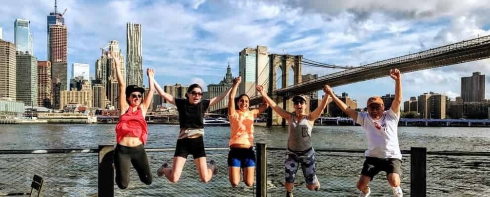 People jumping in front of a city skyline with a bridge in the background. 1