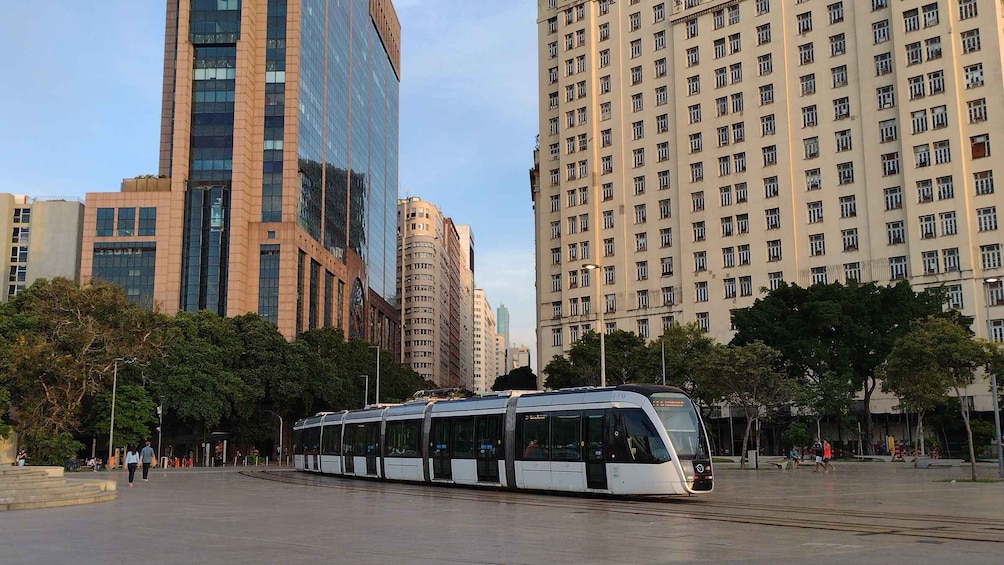 A modern tram moving through a city with tall buildings and trees in the background. 1