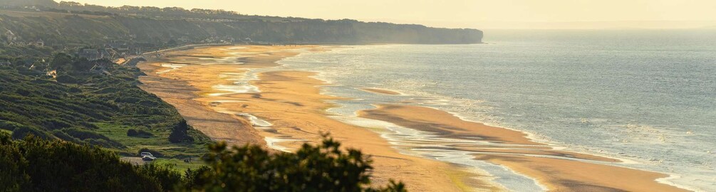 A coastal landscape with a sandy beach, cliffs, and a calm sea. 5