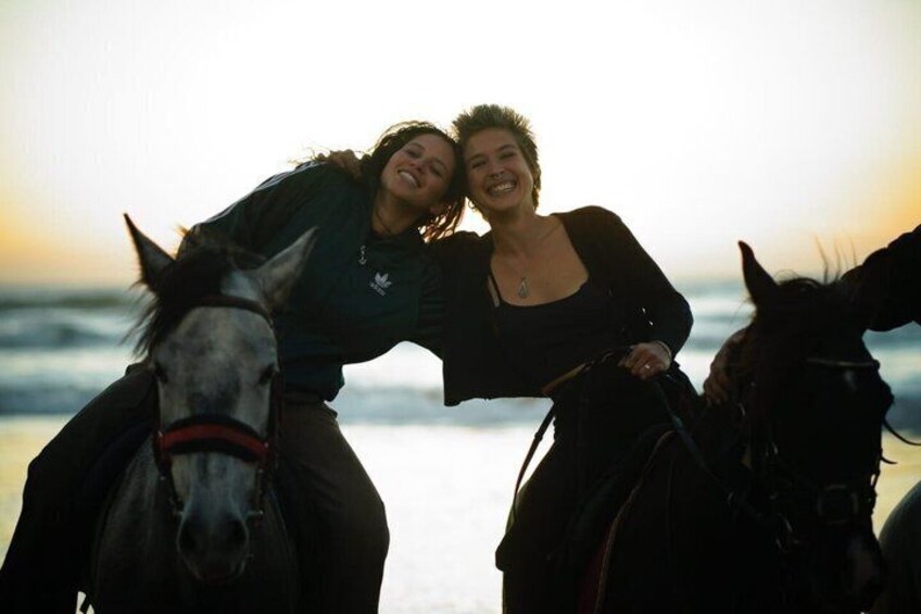 Two people riding horses on a beach with the ocean in the background. 2
