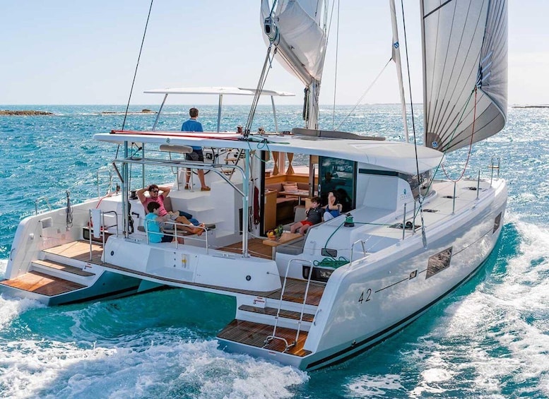 A white catamaran with a cabin and deck seating, sailing on turquoise waters. 2