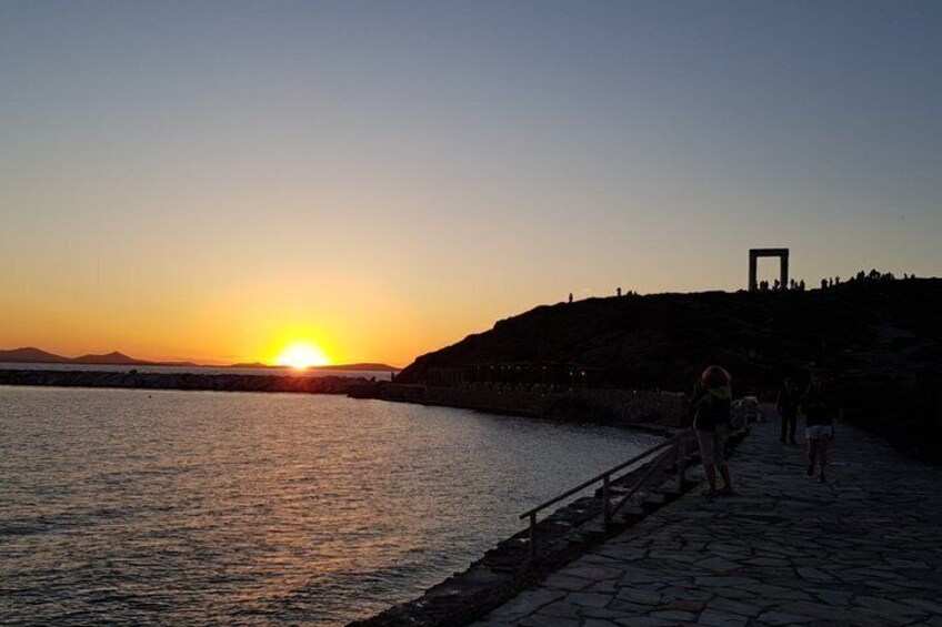 A sunset over a body of water with a stone walkway and a silhouette of people. 2
