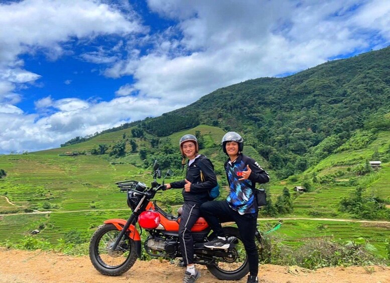 Two people on a motorcycle in a hilly, green landscape with terraced fields. 5