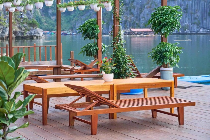 A wooden deck with tables and benches, surrounded by potted plants and overlooking a body of water with boats. 3