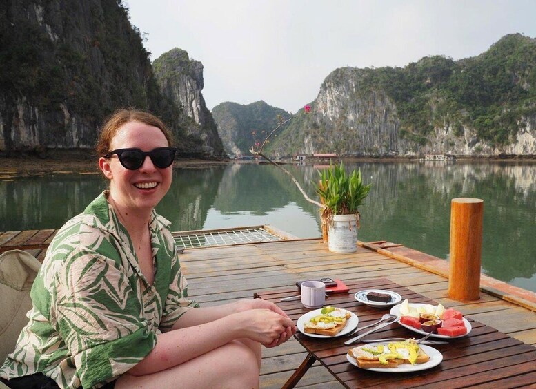 A person sitting on a boat with a table set with food and a potted plant, surrounded by a calm river and rocky cliffs. 5
