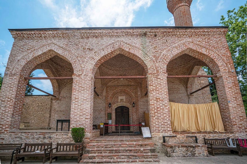 A brick building with three arches, a central door, and a red rope barrier. 2