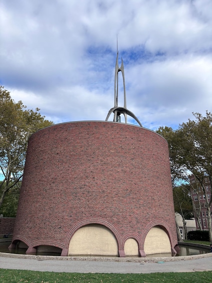 A cylindrical brick structure with a spire, arches, and a pond. 5