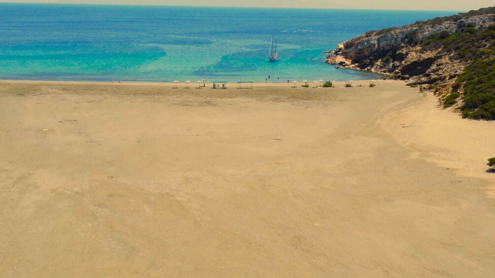 A beach with clear turquoise waters, a sailboat, and rocky cliffs. 5