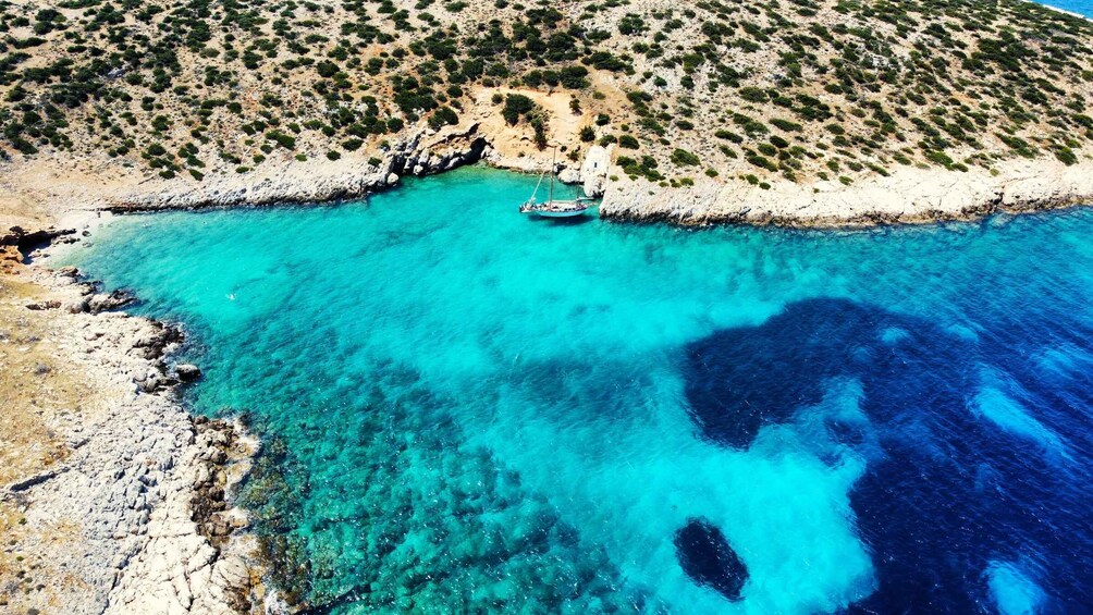 A boat anchored near a rocky coastline with clear turquoise waters. 1