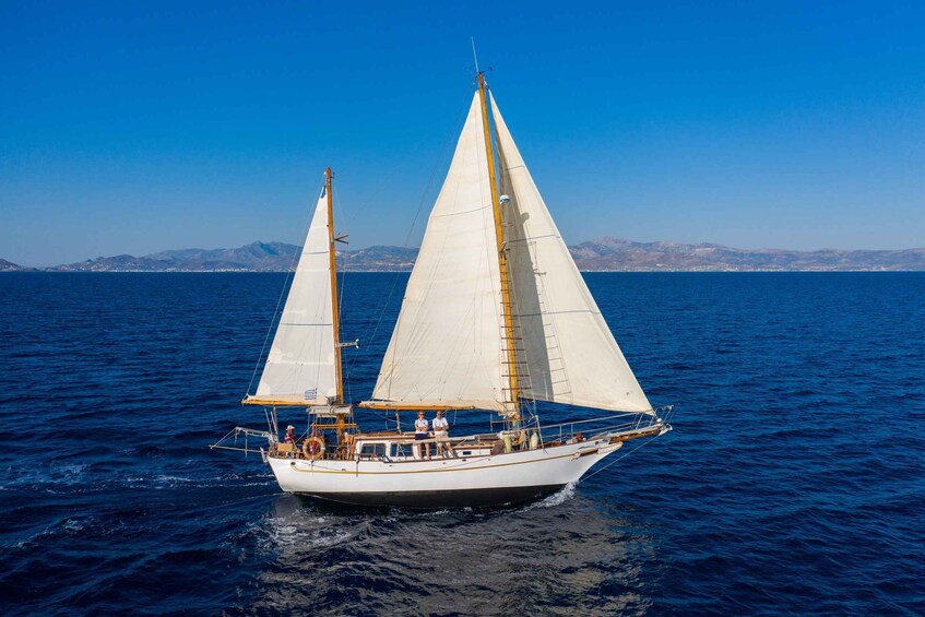 A sailboat with two masts sailing on a calm sea with mountains in the background. 2