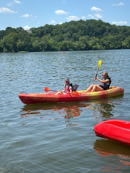 Two people kayaking on a calm lake with a forested hill in the background. 2
