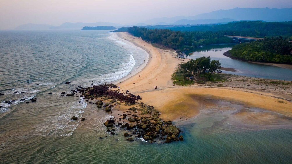 A coastal landscape with a sandy beach, rocky outcrops, and a forested area. 5