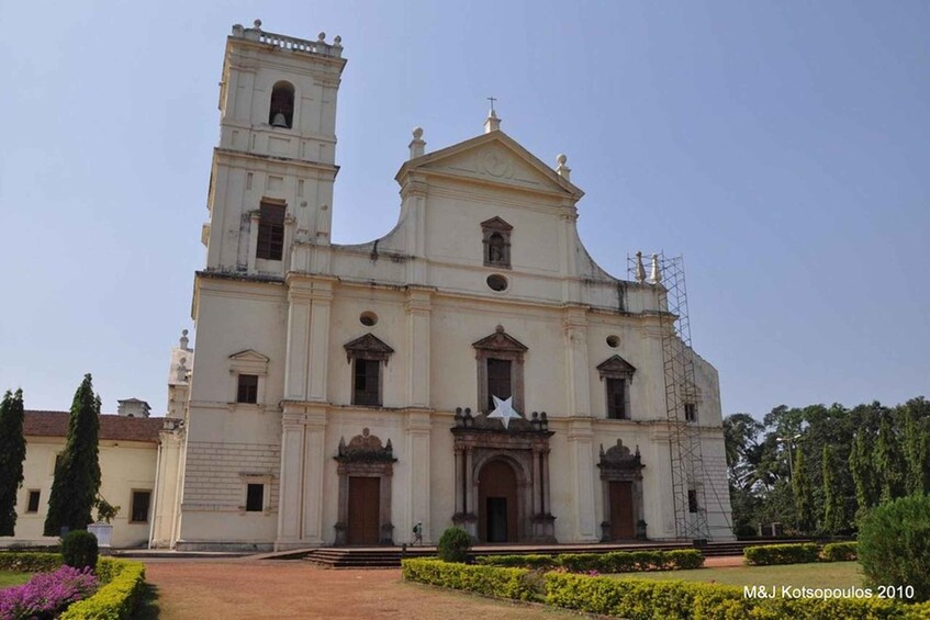 A large, historic church with a bell tower, surrounded by well-maintained gardens and a clear sky. 1