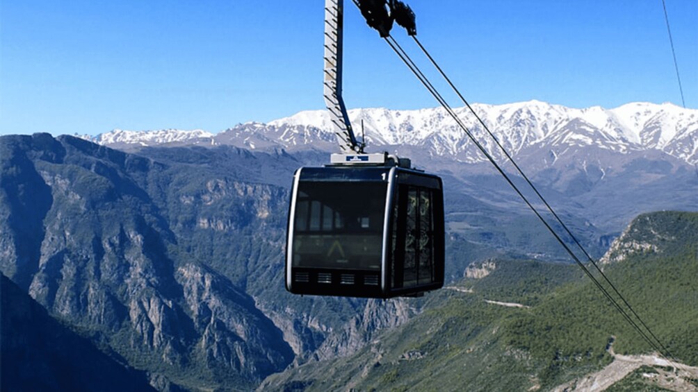 A cable car suspended over a mountainous landscape with snow-capped peaks in the background. 1