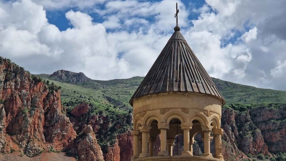 A stone structure with a conical roof and columns, set against a mountainous backdrop. 5