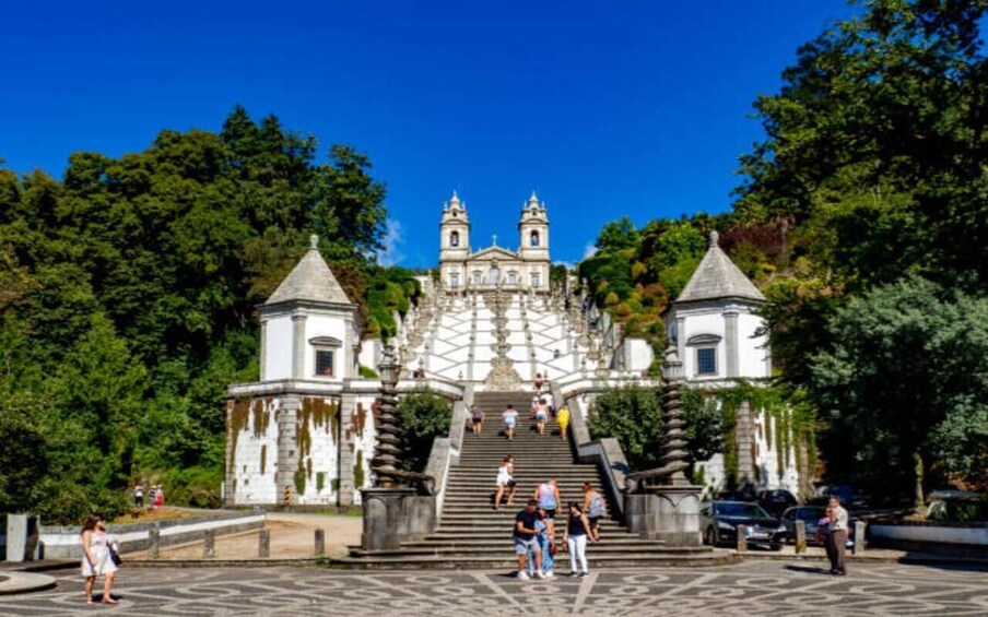 A historic church with a bell tower, surrounded by lush greenery and a paved area with people walking. 1