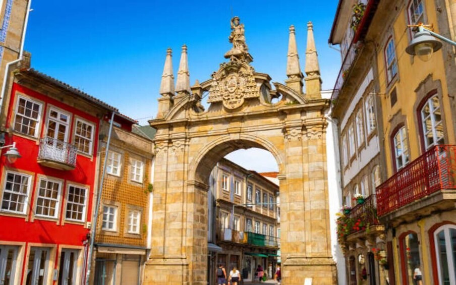 A historic stone archway with intricate carvings and a statue on top, flanked by colorful buildings. 3