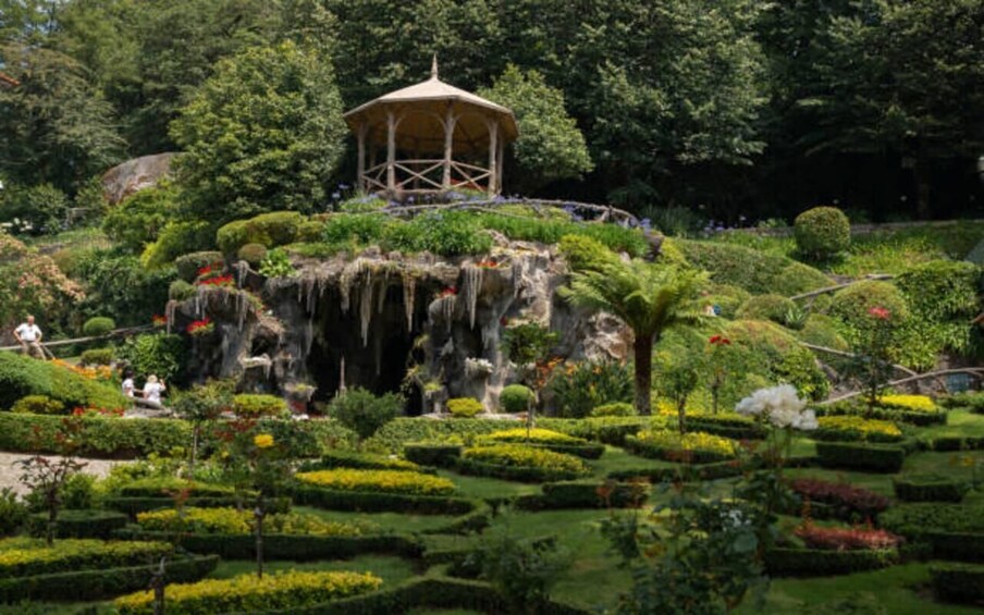 A garden with a gazebo, rock formations, and manicured hedges. 4