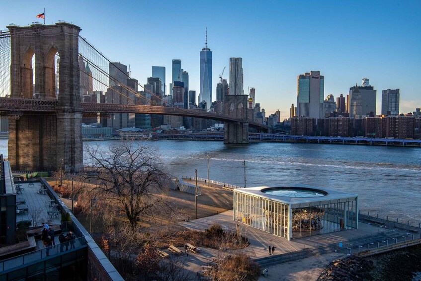 The Brooklyn Bridge, Manhattan skyline, and a glass structure by the river. 1