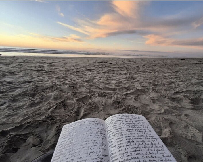 An open book on a sandy beach with a sunset in the background. 3