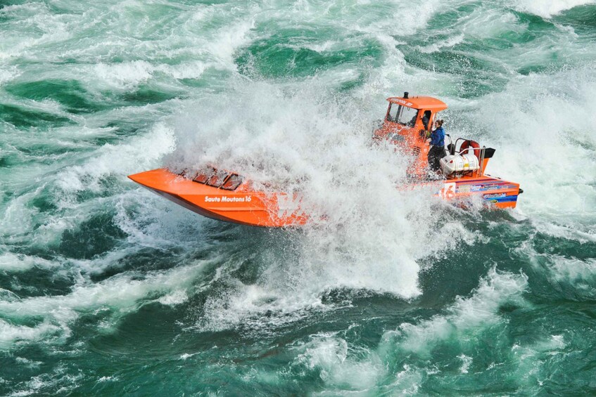 A red speedboat with a person in a blue jacket and another in a white helmet navigating through rough, greenish water. 5