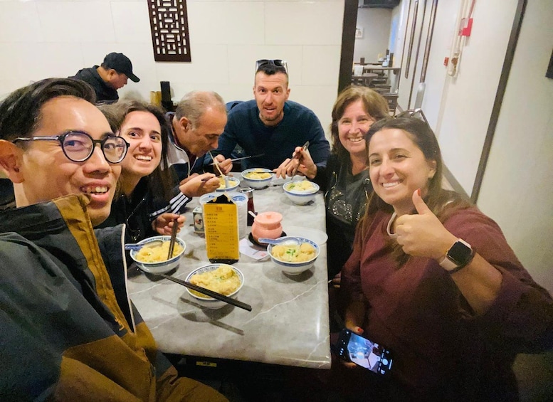 A group of people sitting around a table with bowls of food, engaged in conversation. 4