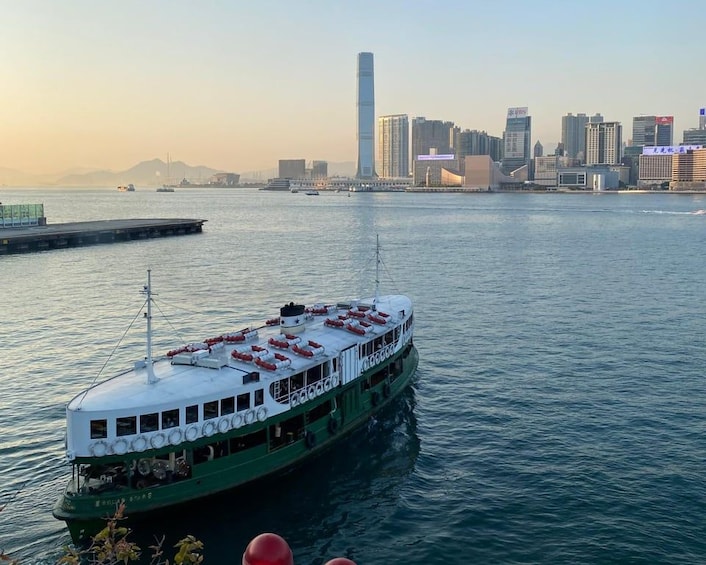 A green riverboat on calm water with a city skyline in the background. 1