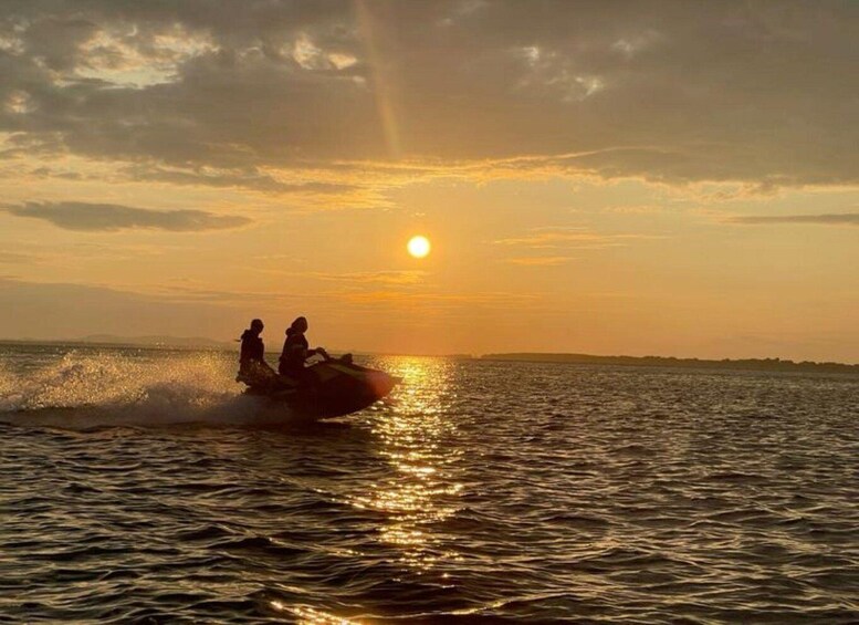 A sunset over a body of water with two people on a jet ski. 2
