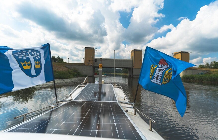 A boat with solar panels, two flags, and a bridge in the background. 2