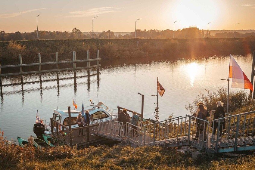 A sunset over a calm river with boats docked, a pedestrian bridge, and a grassy bank. 5