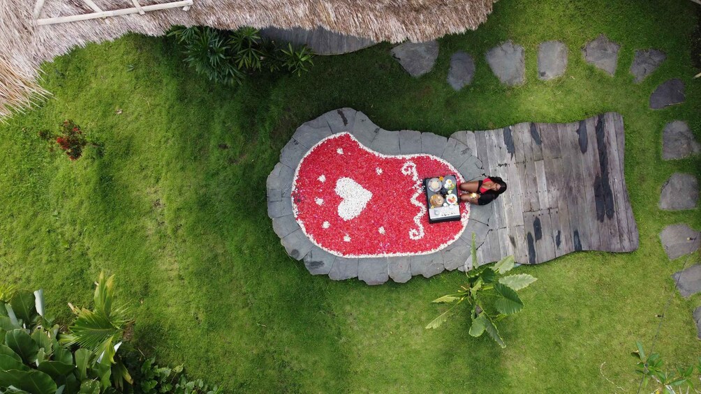 A person standing on a circular stone platform with a heart-shaped flower arrangement, surrounded by grass and plants. 5