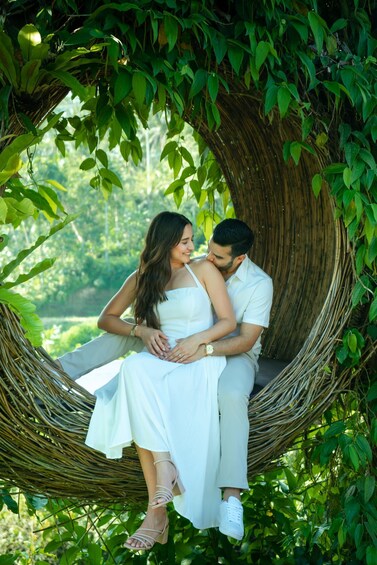 A couple sitting in a wicker swing surrounded by lush greenery. 4