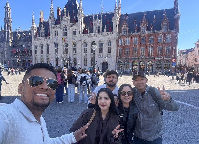 A group of people taking a selfie in front of a historic building with ornate architecture and flags. 3