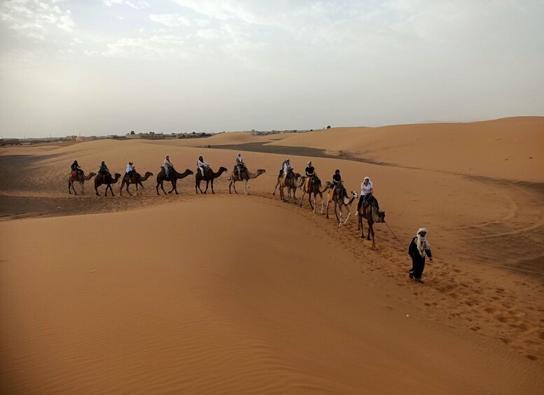 A group of people riding camels across a desert landscape with sand dunes. 4