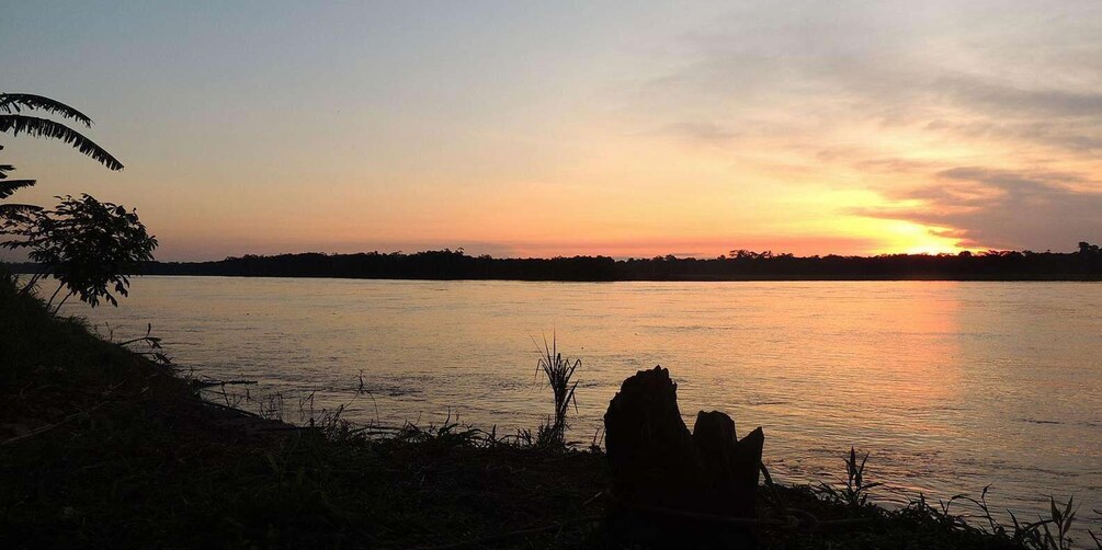 A sunset over a calm river with silhouettes of trees and rocks along the shore. 2