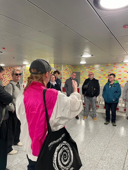 A group of people standing in a subway station with a colorful wall and a ceiling with recessed lighting. 3