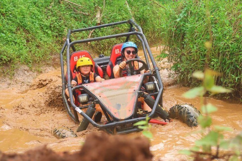 A vehicle navigating a muddy terrain with vegetation on either side. 1