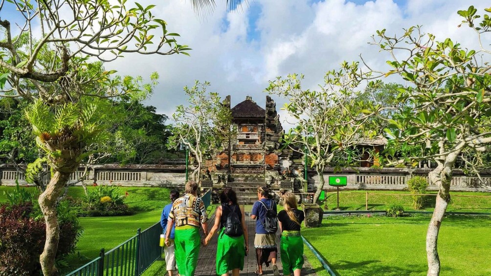 Un groupe de personnes se dirigeant vers un temple balinais traditionnel, doté d’un toit de chaume, entouré d’une végétation luxuriante et sous un ciel dégagé. 1