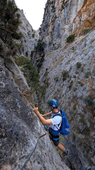 A person climbing a rocky cliff with a blue helmet and backpack. 3