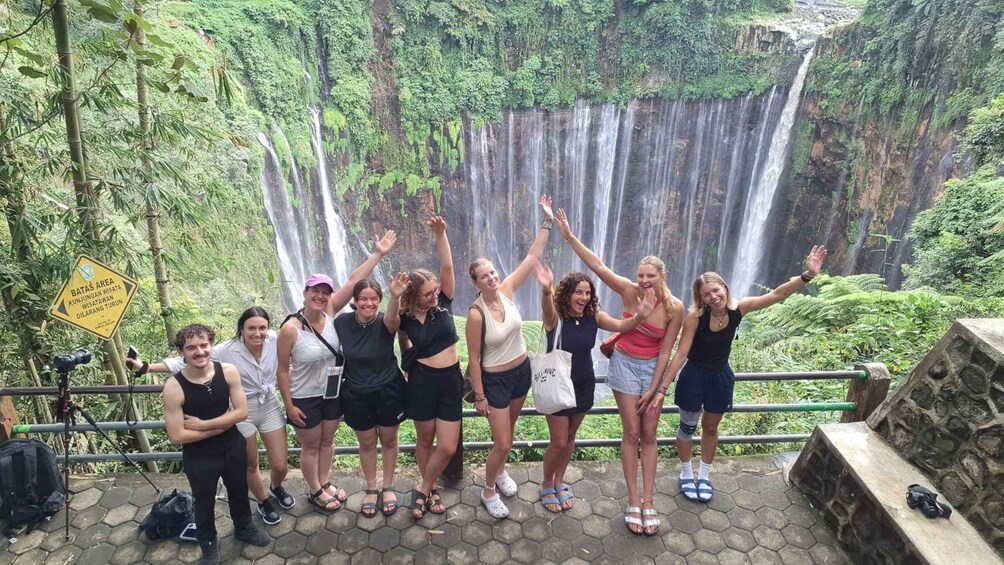 A group of people posing in front of a waterfall with a sign indicating a protected area. 4